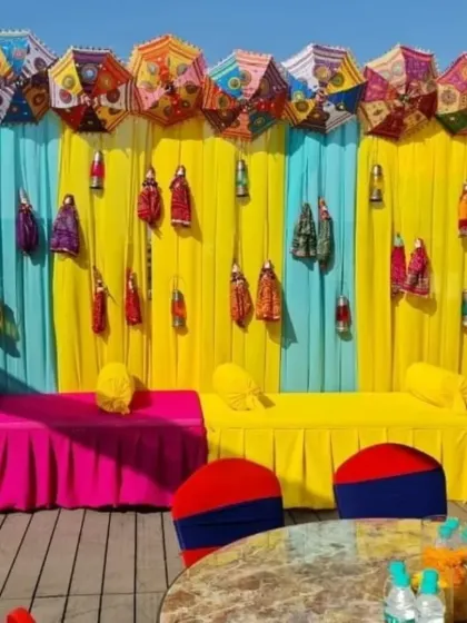 A colorful and quirky Mehendi seating area. The backdrop uses bright yellow and blue drapes, decorated with Rajasthani puppets and embroidered umbrellas for a fun, folk-inspired theme.