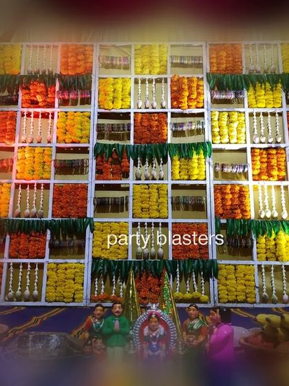 This image shows the floral grid backdrop as part of a larger baby shower setup. In front of the wall of flowers, traditional idols and offerings are placed, integrating the decor seamlessly with the ceremonial proceedings.