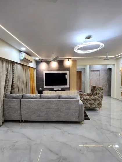 A wide-angle view of a spacious living room project we completed. The design features classic wall molding with gold accents, a large sectional sofa, and a modern TV unit, all under a beautifully lit ceiling.