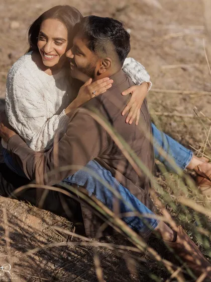 A lovely, relaxed moment of the couple sitting together in a field of dry grass. The warm sunlight and their comfortable embrace create a cozy and romantic atmosphere.