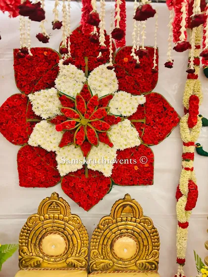A detailed shot of the floral medallion, crafted from red and white flowers, serving as the centerpiece for a wedding backdrop. The two golden chairs await the couple in this traditional setup.