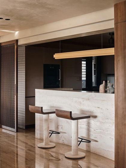 A minimalist bar area featuring a monolithic marble counter and sleek bar stools. A sliding wooden screen allows the space to be either open to the living area or concealed for a cleaner look.