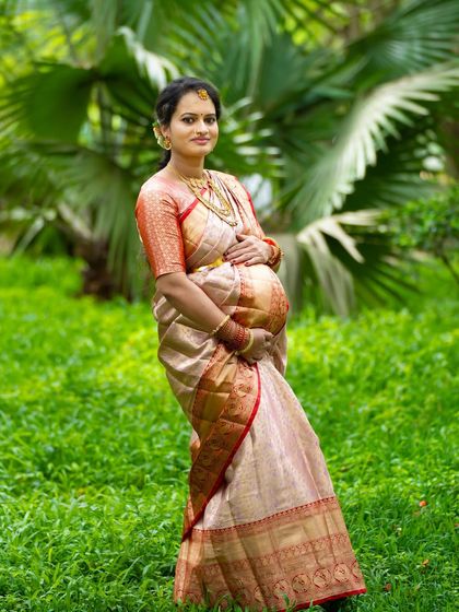A stunning outdoor portrait in a traditional silk saree. The natural green background makes the rich fabric and colors of the saree stand out beautifully.