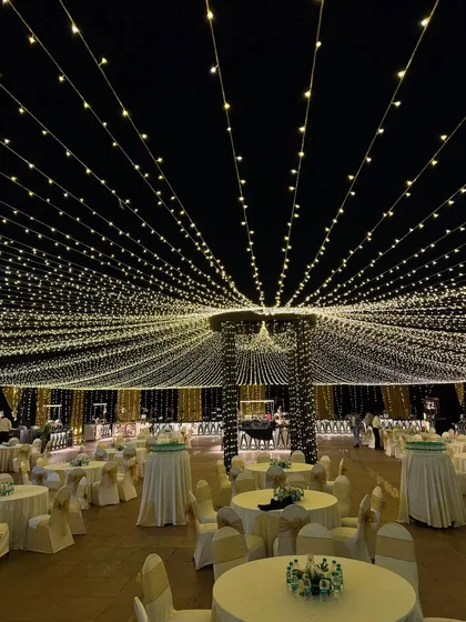An outdoor dining area transformed by a vast ceiling of fairy lights, creating a magical and romantic ambiance for an evening reception.
