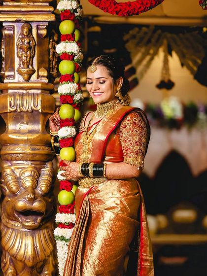 A candid moment of the bride by a decorated pillar. The warm lighting enhances her golden saree and glowing makeup.