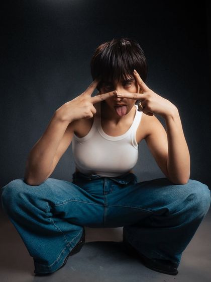 A playful and expressive portrait with a moody, dark backdrop. The model's fun pose contrasts with the dramatic lighting, creating a memorable and personality-driven fashion shot.