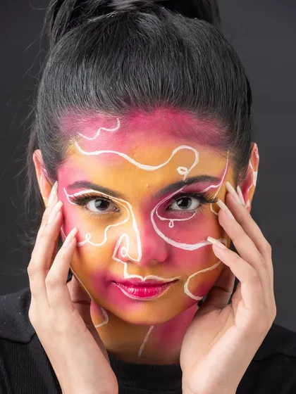 This pose frames the face, drawing attention to the intricate and playful design of the face paint.