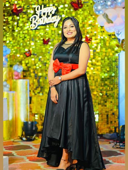 A happy client posing in front of her birthday decorations. The black gown with a red bow is a chic and festive choice.