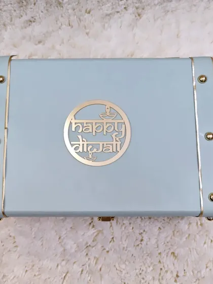 The elegant powder-blue trunk box with a metallic "Happy Diwali" logo. This reusable box is a gift in itself.