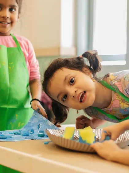 Smiles and splashes of color. Abhyudita and Charlotte are having a blast in their art class, protected by their aprons and free to get creative.