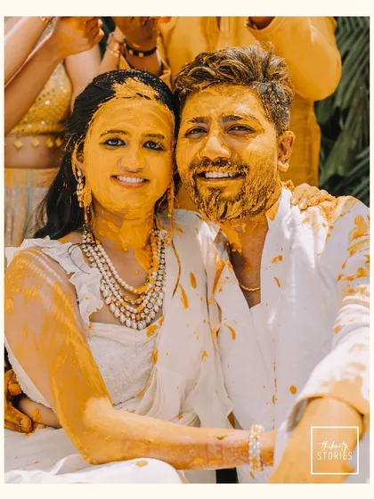 A happy portrait of the couple covered in Haldi paste, smiling for the camera. This image perfectly encapsulates the joyful and messy fun of the ceremony.
