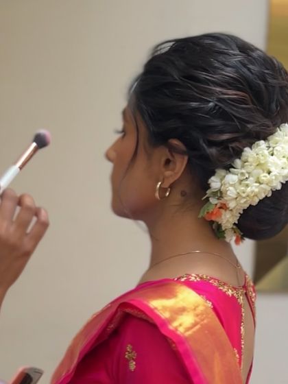 A candid shot of a bride getting her makeup done, with her hair in a soft, textured bun adorned with fresh jasmine.