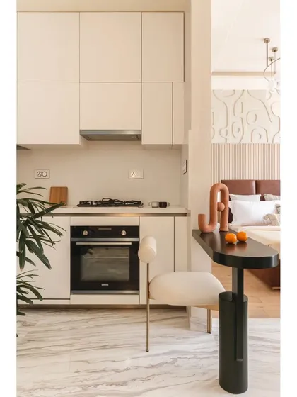 The compact kitchen and dining nook are seamlessly integrated into the open-plan layout. A sleek black table serves as a dining spot, connecting the kitchen to the bedroom area in a fluid, functional way.