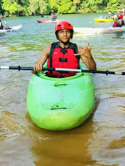 A participant in a green whitewater kayak gives a shaka sign, enjoying the thrill of the Dandeli summer camp.