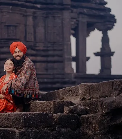 Preet and Gurleen sit together on the ancient stone steps of a temple ruin. The historic setting and their traditional attire create a timeless and powerful image.