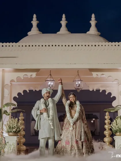 A triumphant moment for the newlyweds against the stunning architecture of their Udaipur wedding venue. The smoke effect and grand setting create a truly cinematic celebration shot.