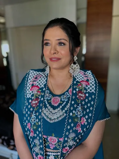 An elegant look for a client in a deep teal embroidered outfit. The makeup is soft and defined, with a classic updo.