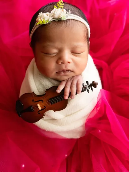A close-up of a peacefully sleeping newborn holding a miniature violin, showcasing how I incorporate unique props to personalize your session.