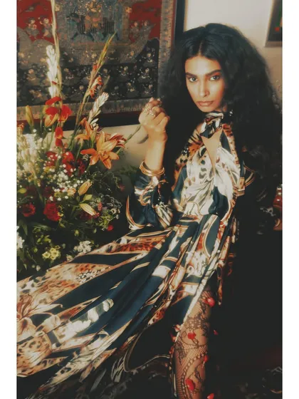 A more composed shot from the same setup. The styling showcases a beautifully printed Rudraksh Dwivedi dress, with the model's pose conveying a sense of quiet strength amidst a floral setting.