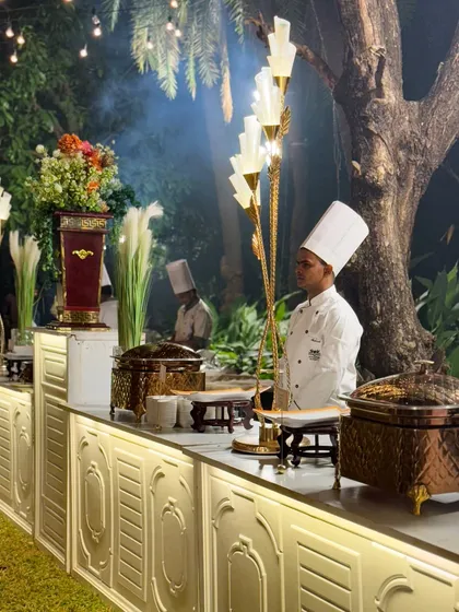 A member of my uniformed staff stands ready at the buffet counter. The combination of professional attire, elegant decor, and high quality serveware ensures a seamless and luxurious guest experience.