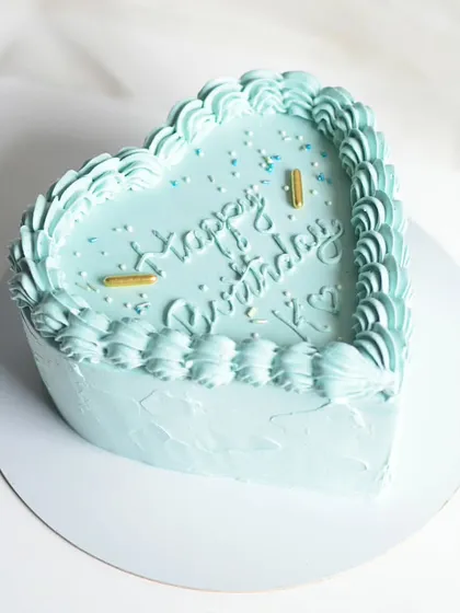 A simple and sweet heart-shaped cake in a lovely pastel blue. The vintage-style piped border and "Happy Birthday" message make it a classic choice for any celebration.