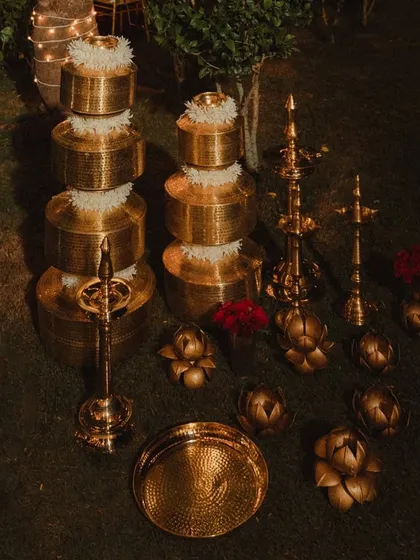 Traditional hammered brass vessels and lotus-shaped candle holders, topped with fresh white flowers. These details were part of the decor for the waterside Varmaala, adding a touch of heritage and light.