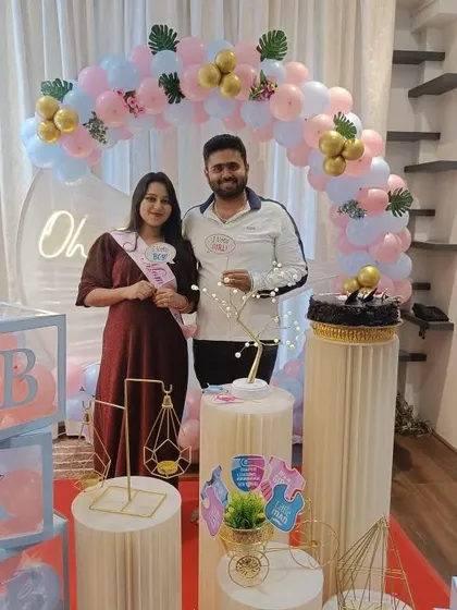 A happy couple at their modern baby shower. The 'He or She' theme is carried through with pink and blue props.