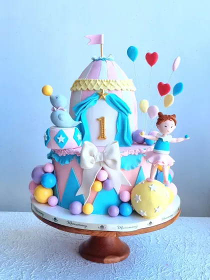Another take on the carnival theme, this time with a pastel color palette. It features a balancing acrobat, a seal, and floating balloons, all sculpted from gumpaste.