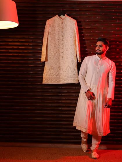 An artistic shot showcasing the groom's anarkali kurta and chudidar alongside the matching cream sherwani. This highlights how I design the complete layered look for your wedding day.