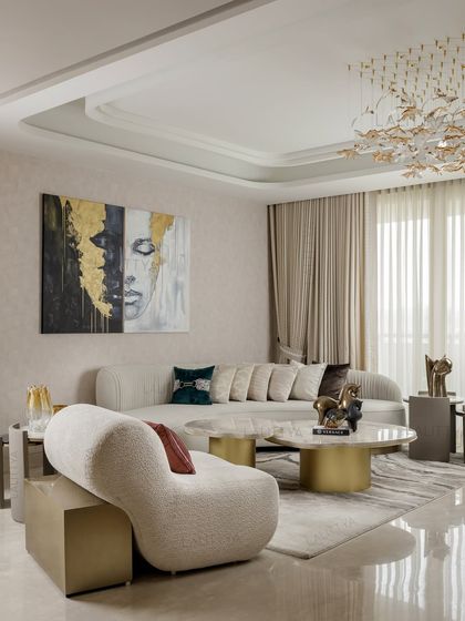 A different angle of the living room, highlighting the sculptural armchair and the play of textures. The combination of a bouclé fabric chair, marble coffee tables, and a plush rug adds depth and tactile interest to the neutral palette.
