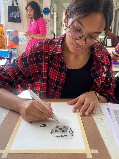 A student uses markers to add detail to a 3D drawing of a dice. We encourage experimentation with different tools and techniques to help students develop their unique artistic style.