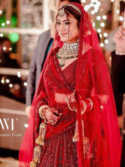 A beautiful bride looking regal in a classic red lehenga, perfectly complemented by our heavy polki choker set with green stone accents. This is a timeless look for any Indian wedding.