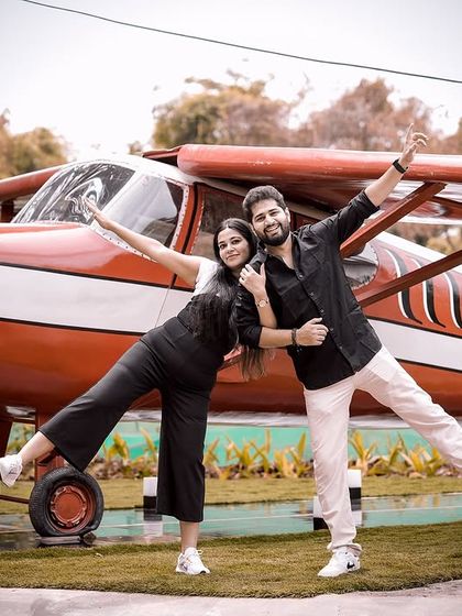 A fun and symmetrical pose in front of a small airplane prop, with the couple striking a playful, wing-like stance.