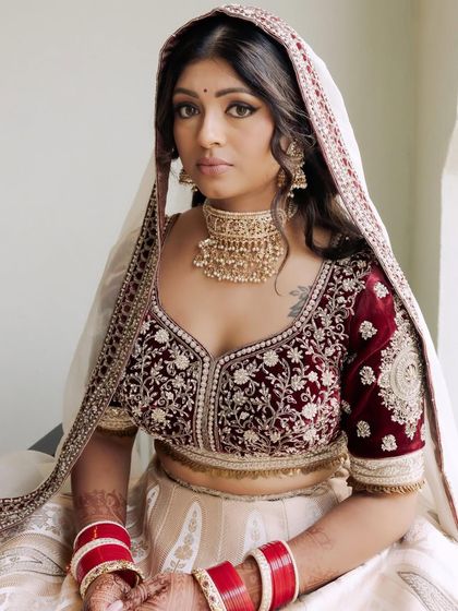 A portrait of Kavi in her stunning bridal attire. The combination of a velvet maroon blouse and an ivory lehenga is unique and beautiful, complemented by her classic makeup.