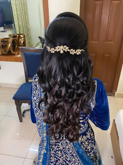 The back view of a reception hairstyle, showing voluminous curls and a half-updo secured with a beautiful gold leafy accessory.