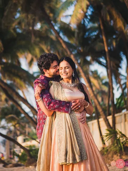 A sweet kiss on the cheek, surrounded by the lush greenery of coastal palm trees. A perfect blend of intimacy and nature.