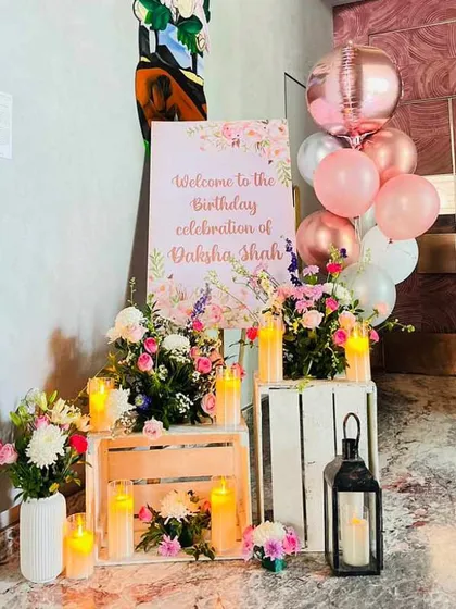 A charming welcome corner for a birthday celebration. We combined a floral welcome sign with fresh flower arrangements on wooden crates, candles, and a bunch of helium balloons.