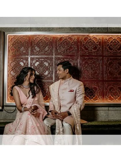 The couple shares an intimate moment, seated against a beautifully lit, ornate wall.