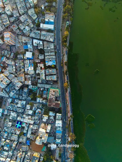 The city of Dahod meets the green waters of a lake. This shot highlights the sharp contrast between the urban environment and the natural landscape it borders.
