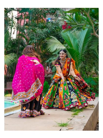 A candid moment of two friends dancing during a Garba shoot. The twirl of the colorful lehenga and their happy interaction showcase the fun and freedom of the dance, creating a lively and dynamic photograph.