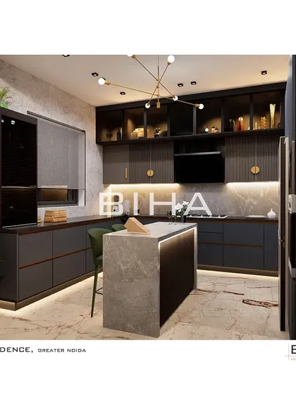 This view of the Greater Noida kitchen showcases the island and the extensive counter space. The design incorporates a built-in oven and microwave tower for ergonomic efficiency, while the brass-accented light fixture adds a sculptural element overhead.