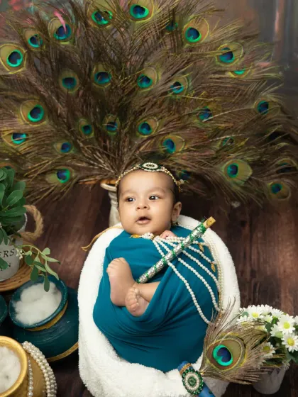 The combination of the teal wrap, peacock feathers, and the baby's alert gaze makes this a truly captivating portrait.