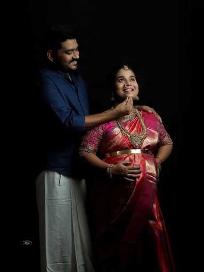 A joyful interaction between a couple during their traditional maternity session. The dark studio background makes their expressions and beautiful attire stand out.