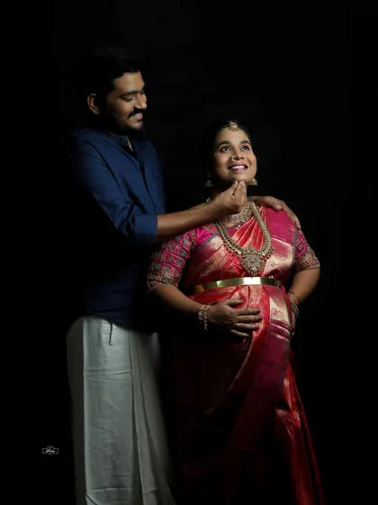 A joyful interaction between a couple during their traditional maternity session. The dark studio background makes their expressions and beautiful attire stand out.