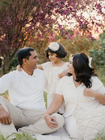 A happy family enjoying a moment together in the park. The coordinated white outfits look beautiful against the natural greenery and pink blossoms.
