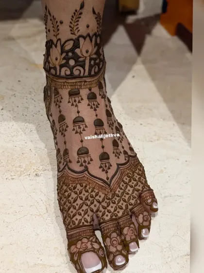 A delicate and modern design for the feet. This pattern features hanging jhumkas and a lotus band at the ankle, creating a jewelry-like effect.