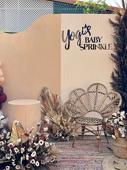 A stylish boho baby sprinkle with a rich, earthy color palette. The decor features a mix of textures, dried florals, a peacock chair, and a modern, two-panel backdrop.