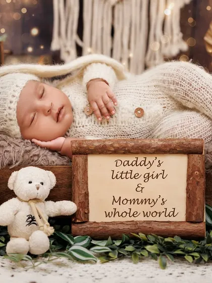 "Daddy's little girl & Mommy's whole world." A newborn sleeps peacefully in a rustic bed setup with a sweet, personalized sign.