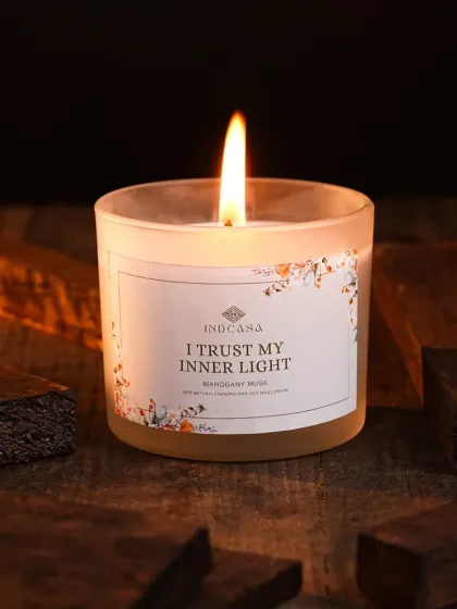 A moody, atmospheric shot of a lit 'Mahogany Musk' candle, styled with dark wood to evoke a sense of warmth and trust. We excel at creating specific moods, from bright and airy to cozy and intimate, for home decor and lifestyle brands.