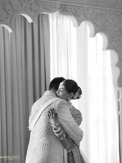 A tender embrace between the bride and groom, framed by an ornate white archway. A timeless black and white moment of love.